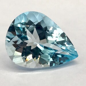 Puede incluir: Una gema de aguamarina facetada en forma de pera. La gema es de color azul claro con múltiples facetas que reflejan la luz. La piedra se encuentra sobre un fondo blanco, lo que resalta su claridad y brillo. Es una hermosa piedra preciosa.