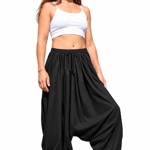 Op de afbeelding: Een wit crop topje met spaghettibandjes en een wijde zwarte harembroek met een elastische tailleband en een trekkoord. De broek heeft een verlaagd kruis en elastische boorden bij de enkels, wat zorgt voor een volumineus silhouet.