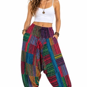 Op de afbeelding: Losvallende harembroek met een levendig patchworkontwerp van veelkleurige verticale strepen in tinten rood, blauw, groen en geel. De broek heeft een elastische tailleband met een trekkoord en elastische boorden bij de enkels.