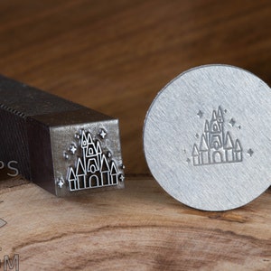 May include: A metal stamp with a design of a castle with stars. The stamp is on a wooden surface. The text "STAMPS" is visible on the handle of the stamp.