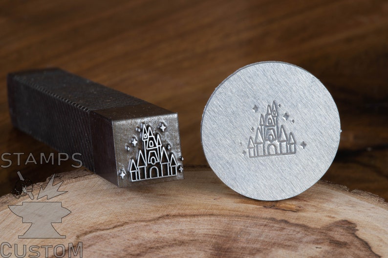 May include: A metal stamp with a design of a castle with stars. The stamp is on a wooden surface. The text "STAMPS" is visible on the handle of the stamp.