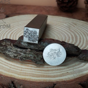 May include: Two metal stamps with a wolf head design. The stamps are on a wooden surface.