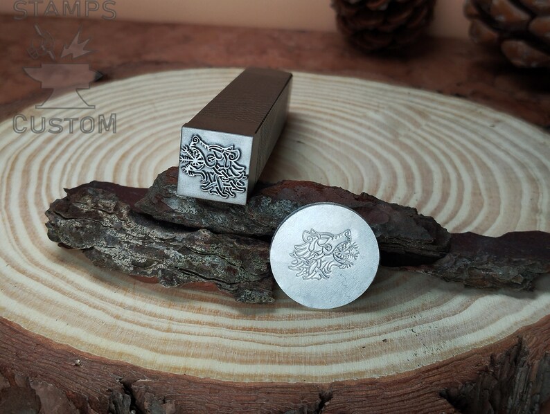 May include: Two metal stamps with a wolf head design. The stamps are on a wooden surface.