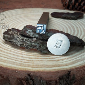 May include: Two metal stamps with the Chinese character "后" (meaning "after") on a wooden surface. The stamps are used for creating impressions in metal.