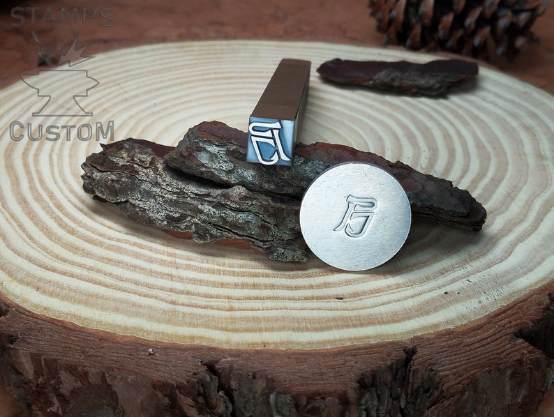 May include: Two metal stamps with the Chinese character "后" (meaning "after") on a wooden surface. The stamps are used for creating impressions in metal.