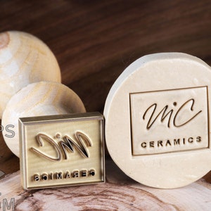 May include: Two brass stamps with wooden handles. The stamp on the left has the text "JIM" and "SOIMAGERS" engraved on it. The stamp on the right has the text "MIC CERAMICS" and a handwritten logo engraved on it.