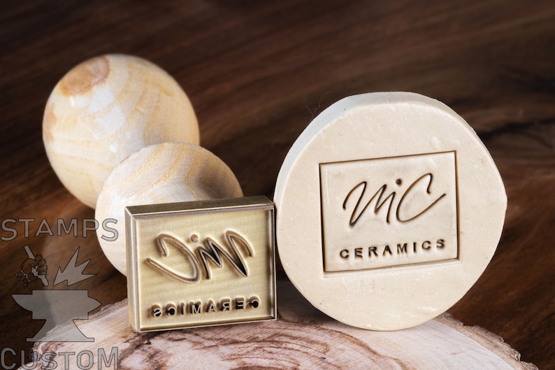 May include: Two brass stamps with wooden handles. The stamp on the left has the text "JIM" and "SOIMAGERS" engraved on it. The stamp on the right has the text "MIC CERAMICS" and a handwritten logo engraved on it.