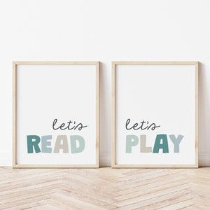 May include: Two framed prints with the text "let's read" and "let's play" in colorful, stylized lettering. The prints are in wooden frames and are hung on a white wall.