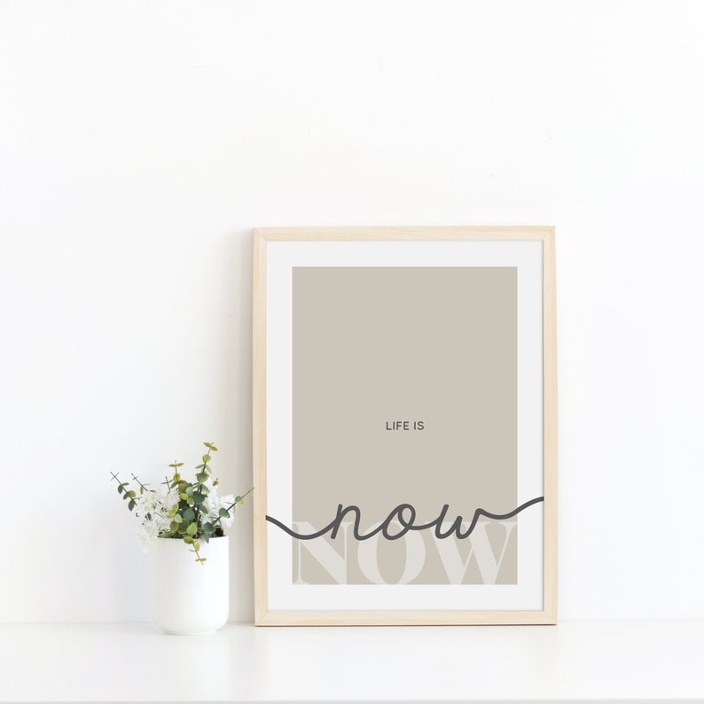 Może przedstawiać: Wydruk w ramie z beżowym tłem i tekstem "LIFE IS NOW" w czerni i bieli. Słowo "NOW" jest napisane kursywą i częściowo zasłonięte czarną linią.