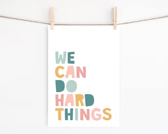 Puede incluir: Una impresión colorida con el texto "WE CAN DO HARD THINGS" en un formato escalonado y apilado. Las palabras están en varios tonos de azul, rosa y amarillo.