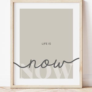 Może przedstawiać: Wydruk w ramie z beżowym tłem i tekstem "LIFE IS NOW" w czerni i bieli. Słowo "NOW" jest napisane kursywą.