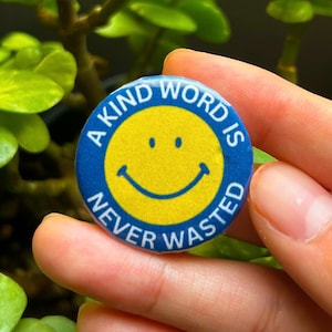 May include: A blue and yellow button with a smiley face and the text "A kind word is never wasted".