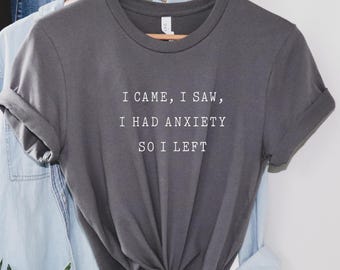 May include: A gray t-shirt with the text "I came, I saw, I had anxiety so I left" printed in white.