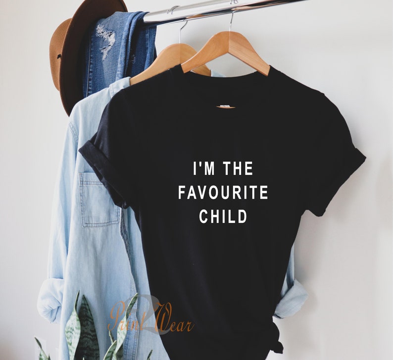 Peut inclure: T-shirt noir avec un texte blanc qui dit "Je suis l'enfant pr&eacute;f&eacute;r&eacute;".