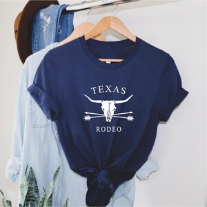 May include: A navy blue t-shirt with a white graphic of a steer skull with crossed arrows and the text "TEXAS RODEO".