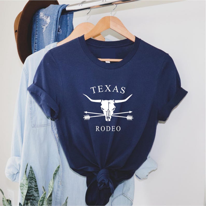May include: A navy blue t-shirt with a white graphic of a steer skull with crossed arrows and the text "TEXAS RODEO".
