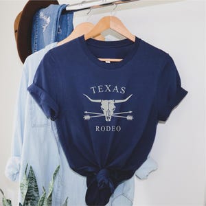 May include: A navy blue t-shirt with a white graphic of a steer skull with crossed arrows and the text "TEXAS RODEO".