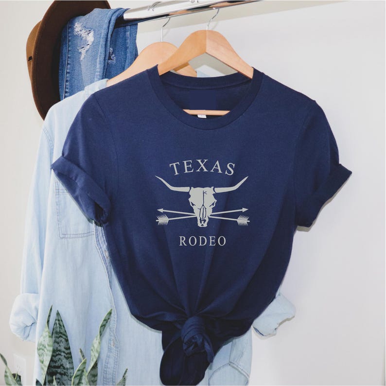 May include: A navy blue t-shirt with a white graphic of a steer skull with crossed arrows and the text "TEXAS RODEO".