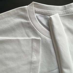 May include: A white t-shirt folded in half, showing the neckline and a seam on the sleeve.