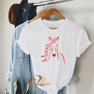K&ouml;nnte beinhalten: Wei&szlig;es T-Shirt mit einem roten Pferdekopf-Motiv. Die M&auml;hne des Pferdes weht im Wind.