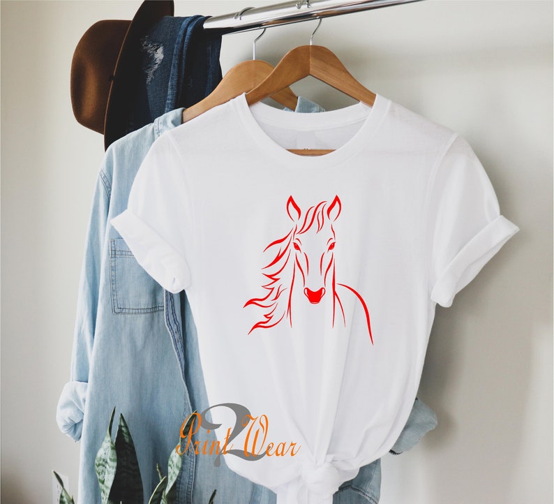 K&ouml;nnte beinhalten: Wei&szlig;es T-Shirt mit einem roten Pferdekopf-Motiv. Die M&auml;hne des Pferdes weht im Wind.