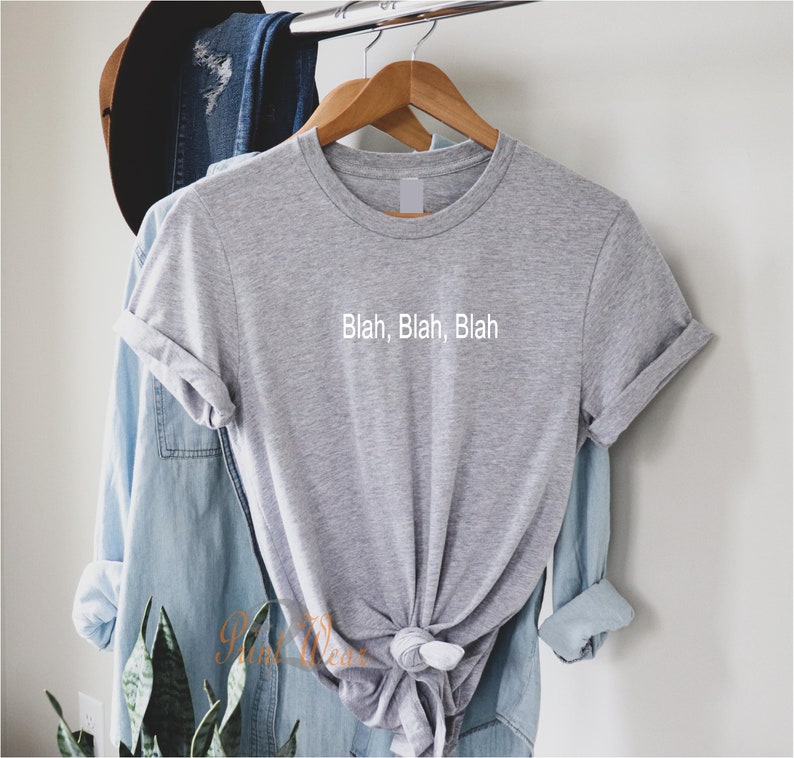 May include: A gray t-shirt with the text "Blah, Blah, Blah" printed on the front. The shirt is hanging on a wooden hanger.