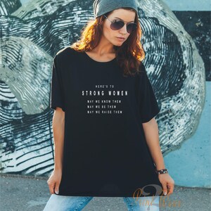 May include: Black t-shirt with white text that reads "Here's to Strong Women. May we know them. May we be them. May we raise them."