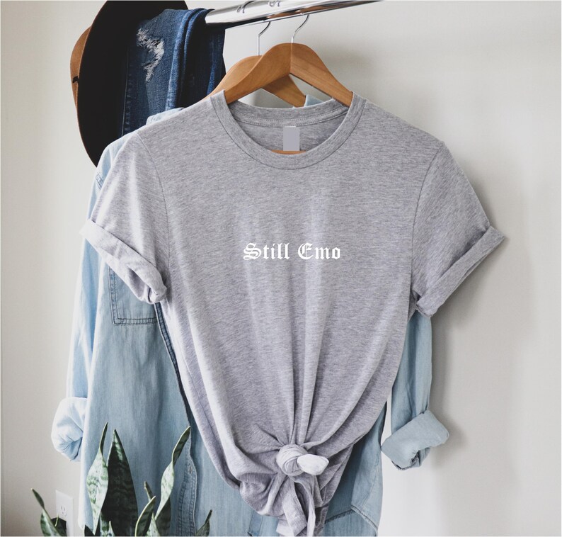 May include: Gray short-sleeved t-shirt with the text "Still Emo" in white lettering.