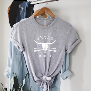 May include: Gray t-shirt with a white graphic of a bull skull with crossed arrows and the text "TEXAS RODEO".