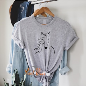 K&ouml;nnte beinhalten: Ein graues T-Shirt mit einer schwarzen Umrandung eines Pferdekopfes auf der Vorderseite.