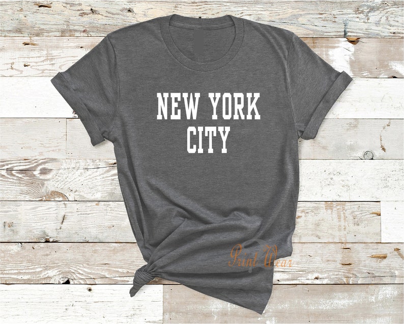 Puede incluir: Una camiseta gris oscura con el texto "NEW YORK CITY" impreso en blanco.