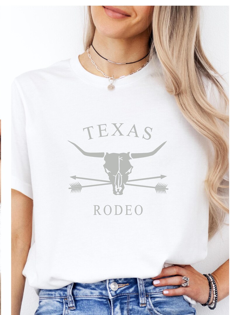 May include: White t-shirt with a gray graphic design featuring a bull skull with crossed arrows and the text "TEXAS RODEO".