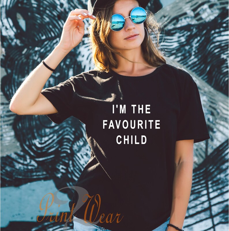 Peut inclure: Un t-shirt noir avec du texte blanc qui dit "Je suis l'enfant pr&eacute;f&eacute;r&eacute;".