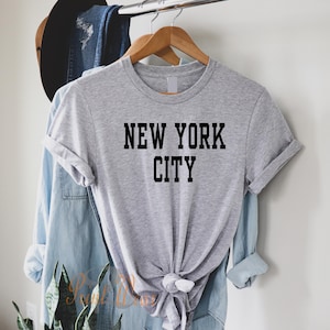 Puede incluir: Camiseta gris con texto negro que dice "NEW YORK CITY".