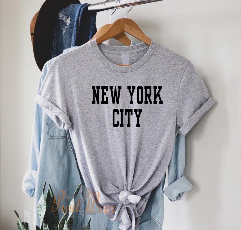 Puede incluir: Camiseta gris con texto negro que dice "NEW YORK CITY".