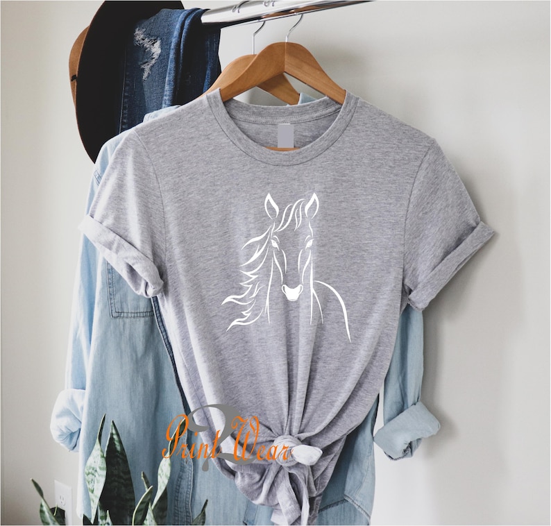 K&ouml;nnte beinhalten: Ein graues T-Shirt mit einer wei&szlig;en Umrandung eines Pferdekopfes auf der Vorderseite.