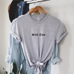 May include: A gray t-shirt with the text "Still Emo" in black gothic lettering.