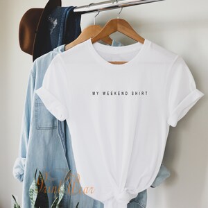 May include: White t-shirt with the text "MY WEEKEND SHIRT" printed in black on the front.