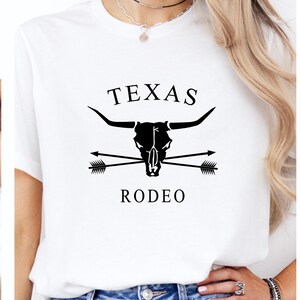May include: White t-shirt with a black graphic design featuring a bull skull with crossed arrows and the text "TEXAS RODEO".