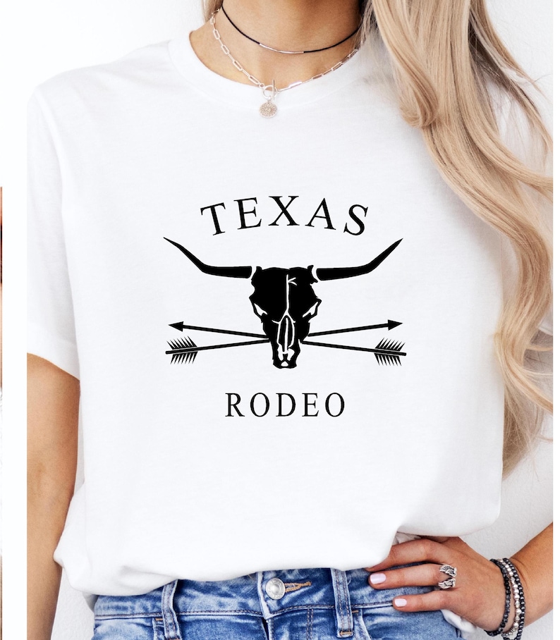 May include: White t-shirt with a black graphic design featuring a bull skull with crossed arrows and the text "TEXAS RODEO".