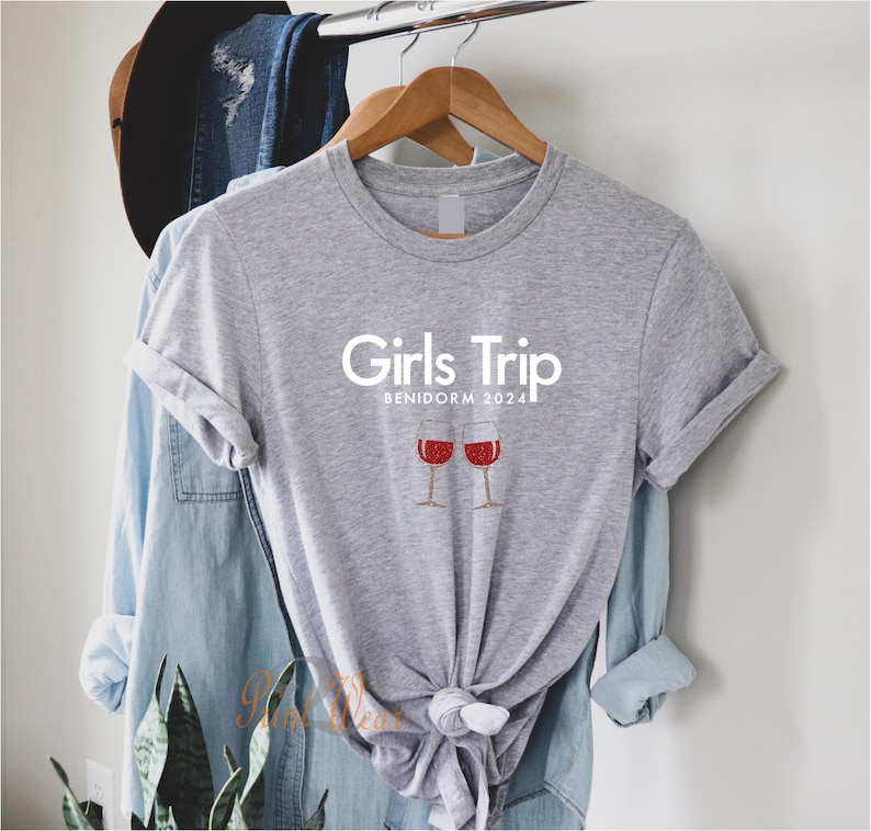 Pode incluir: Camiseta cinza com o texto "Girls Trip Benidorm 2024" e um gr&aacute;fico de duas ta&ccedil;as de vinho com vinho tinto.