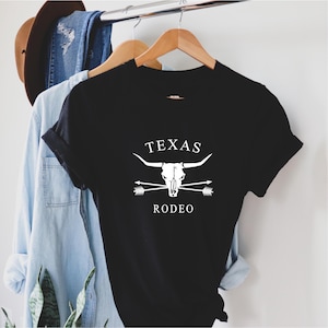 May include: Black t-shirt with a white graphic design of a bull skull with crossed arrows and the text "TEXAS RODEO".
