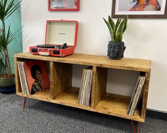 May include: A rustic wooden record player stand with three shelves, featuring a red record player and a potted plant. The stand has copper-coloured hairpin legs and is displayed on a grey carpet.