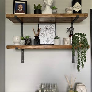 a wooden shelf with various decorative items and plants, including a framed photo, a bust, and several potted plants.