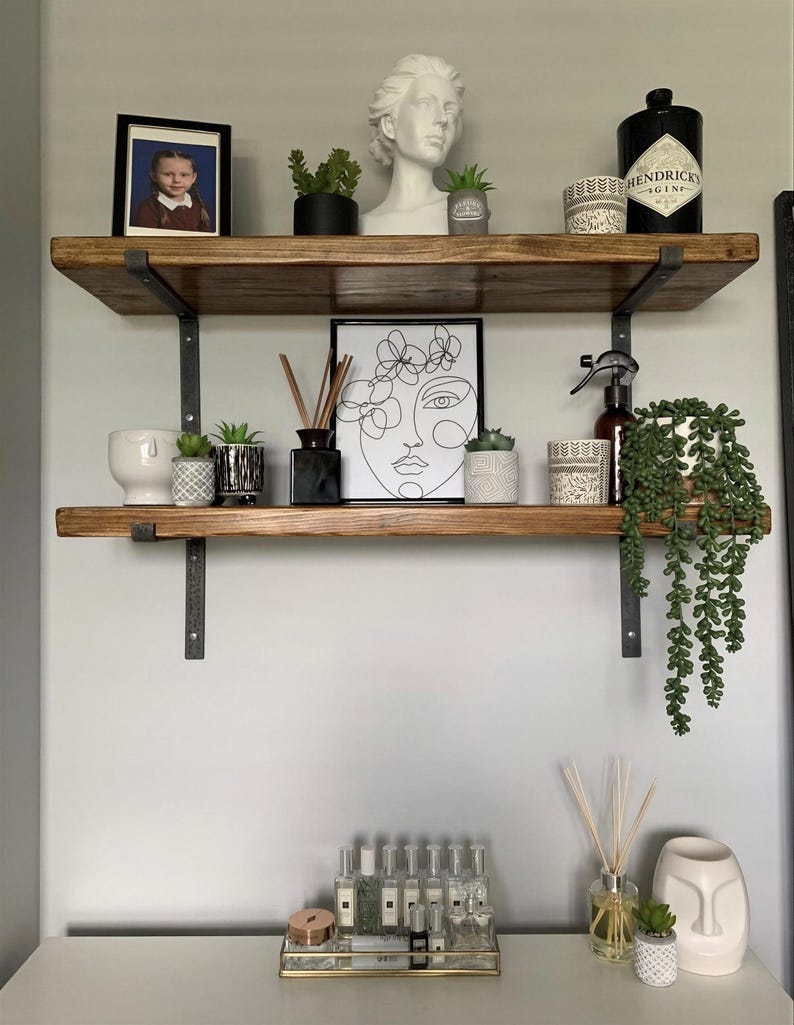 a wooden shelf with various decorative items and plants, including a framed photo, a bust, and several potted plants.