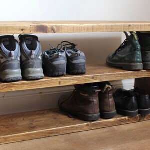 May include: A wooden shoe rack with two shelves. The top shelf has three pairs of hiking boots and the bottom shelf has three pairs of brown boots and two pairs of black boots.