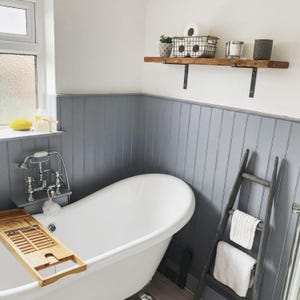 a bathroom with a white freestanding bathtub, a wooden tray, and a shelf with various toiletries and decorative items.