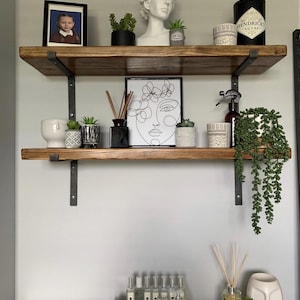 a wooden shelf with various decorative items and plants, including a framed photo, a bust, and several potted plants.
