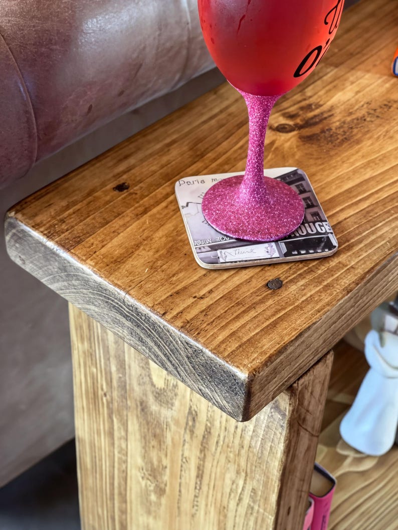 A pink glittery wine glass sits on a wooden table, with a coaster underneath.