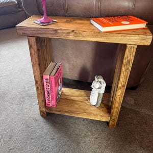 A wooden side table with a pink wine glass and a book on it, placed in a living room setting with a brown leather couch in the background.